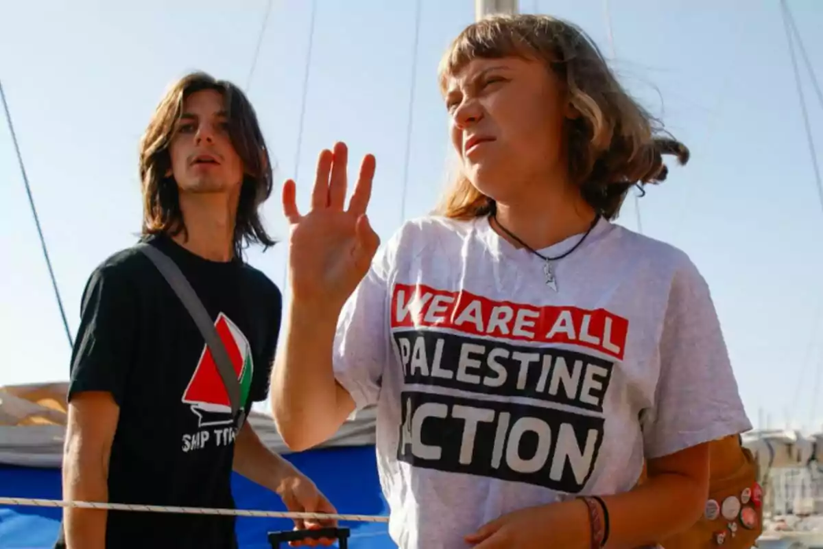 Dos personas jóvenes están al aire libre, una de ellas lleva una camiseta con el mensaje We are all Palestine Action y la otra una camiseta negra con un gráfico y la frase Ship to, ambas parecen participar en una actividad o protesta. Dos personas jóvenes están al aire libre, una de ellas lleva una camiseta con el mensaje We are all Palestine Action y la otra una camiseta negra con un gráfico y la frase Ship to, ambas parecen participar en una actividad o protesta.