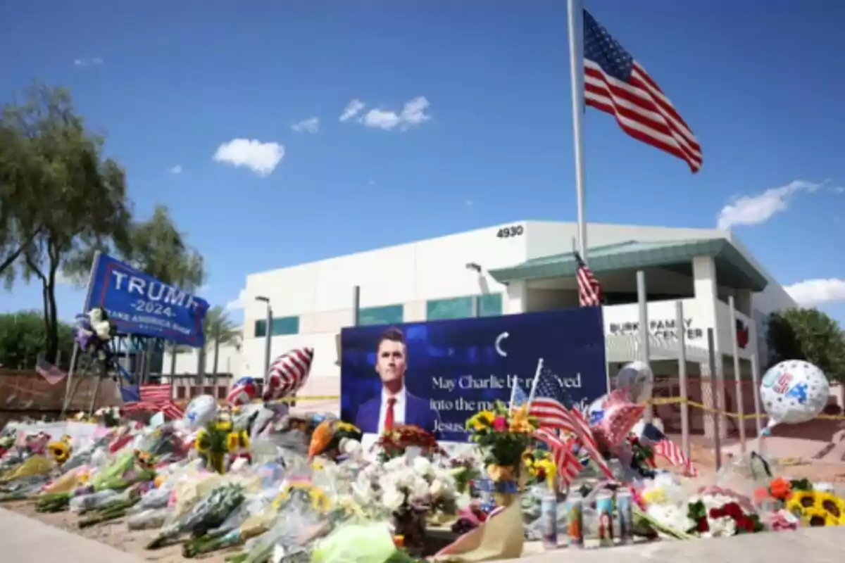 Flores, banderas y globos se acumulan en un memorial a Charlie Kirk frente a un edificio con una bandera de Estados Unidos a media asta y un cartel de campaña de Trump 2024. Flores, banderas y globos se acumulan en un memorial a Charlie Kirk frente a un edificio con una bandera de Estados Unidos a media asta y un cartel de campaña de Trump 2024.