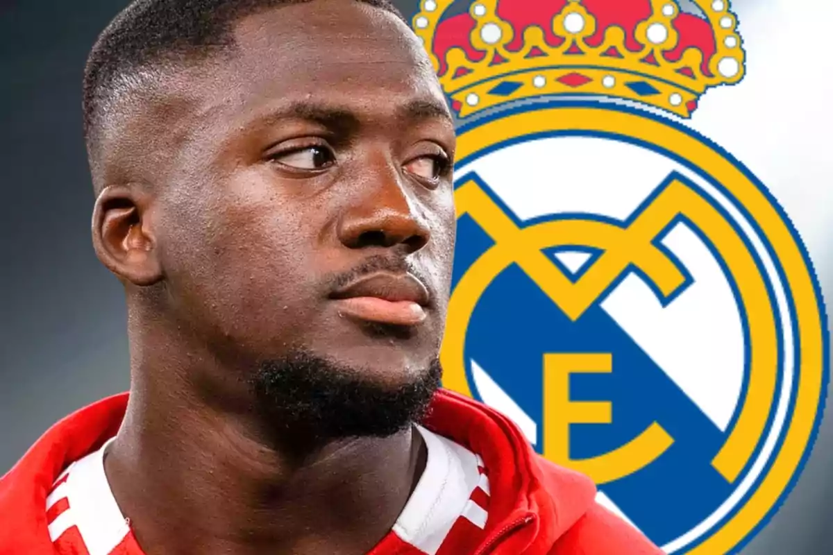 Un futbolista amb jaqueta vermella apareix en primer pla mentre al fons s’observa l’escut del Reial Madrid.