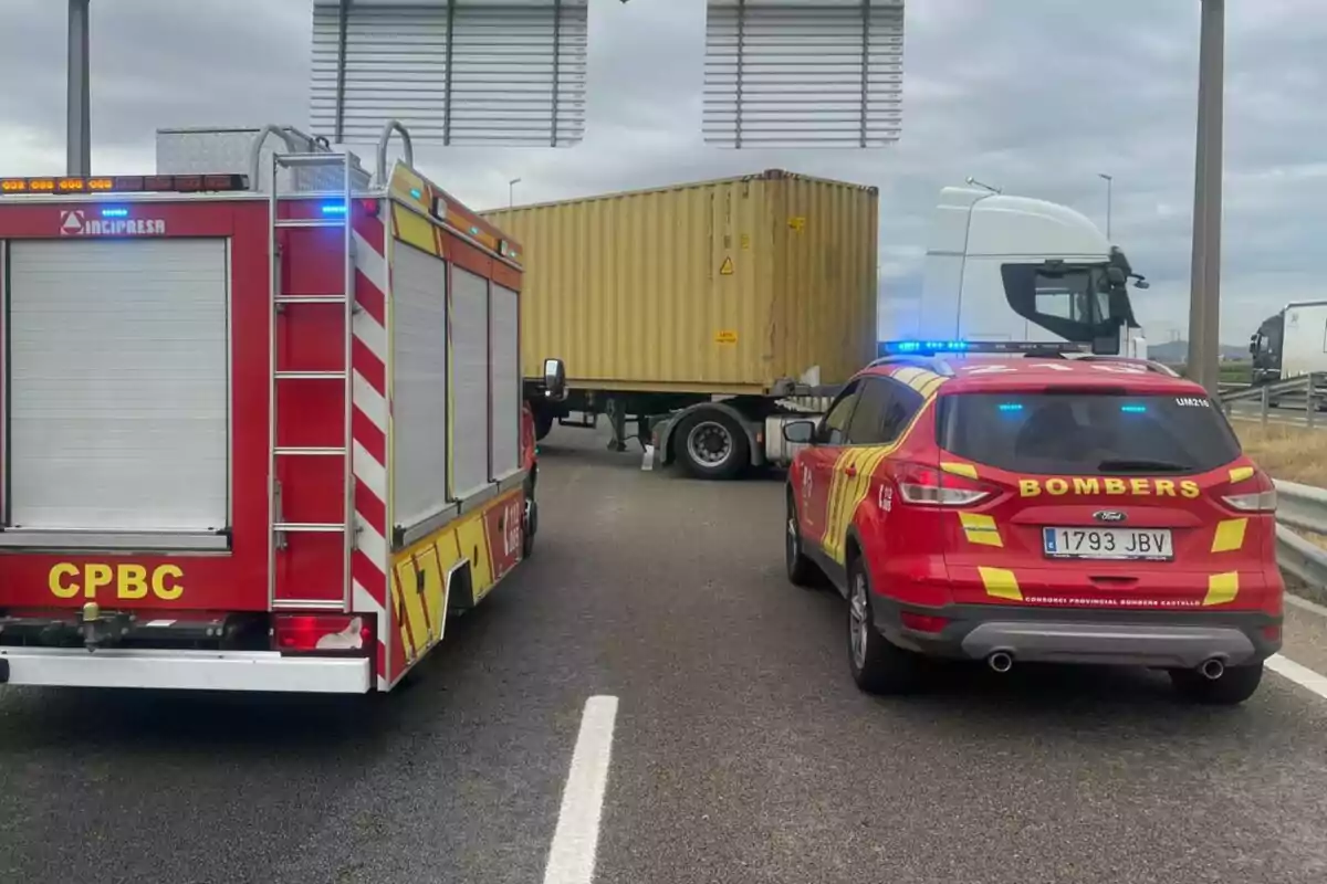 Un camió de bombers i un vehicle d’emergència bloquegen una carretera al costat d’un tràiler amb contenidor groc aturat al mig de l’asfalt. Un camió de bombers i un vehicle d’emergència bloquegen una carretera al costat d’un tràiler amb contenidor groc aturat al mig de l’asfalt.