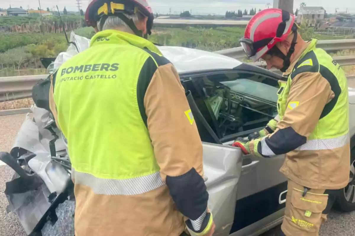 Dos bombers revisen un cotxe platejat que ha patit un accident en una carretera.