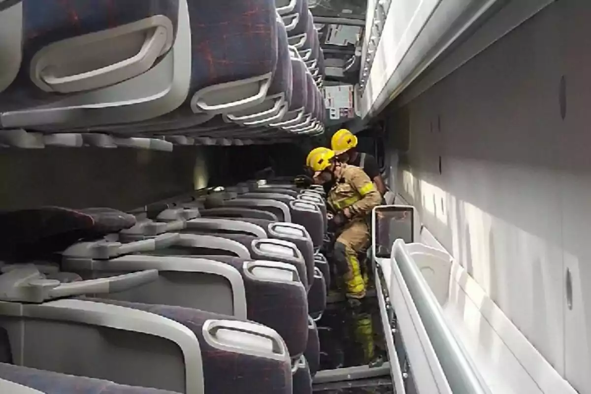 Dos bombers amb casc groc revisen l’interior inclinat d’un autobús de passatgers buit