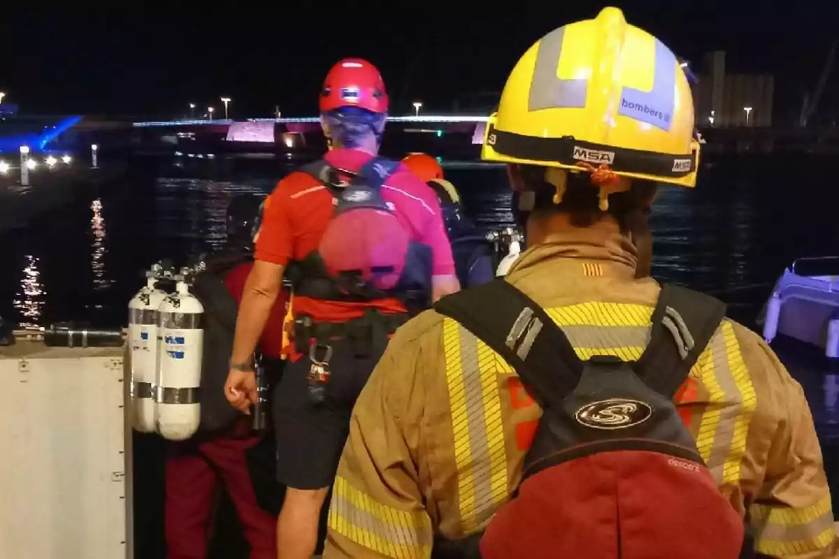 Varios bomberos con equipo de rescate acuático se preparan junto a un muelle durante la noche Varios bomberos con equipo de rescate acuático se preparan junto a un muelle durante la noche