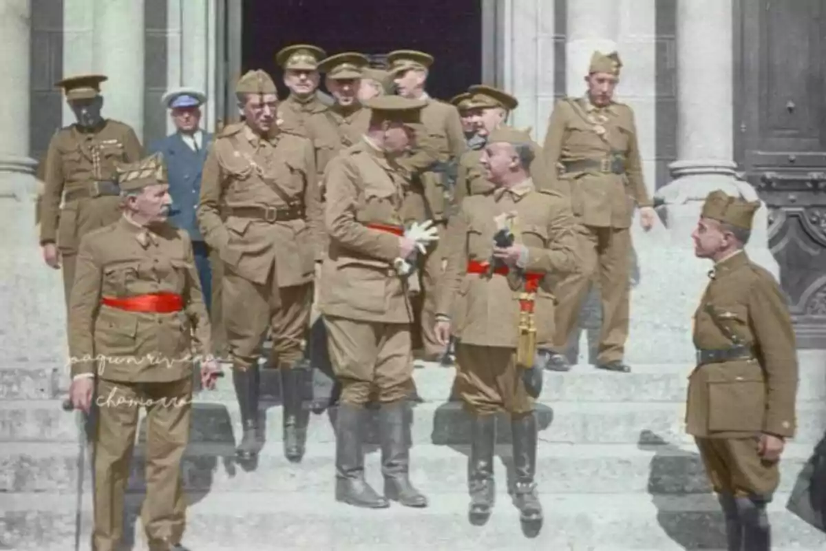 Un grup de militars amb uniformes marrons i cinturons vermells conversa a les escales d’un edifici de pedra amb columnes.