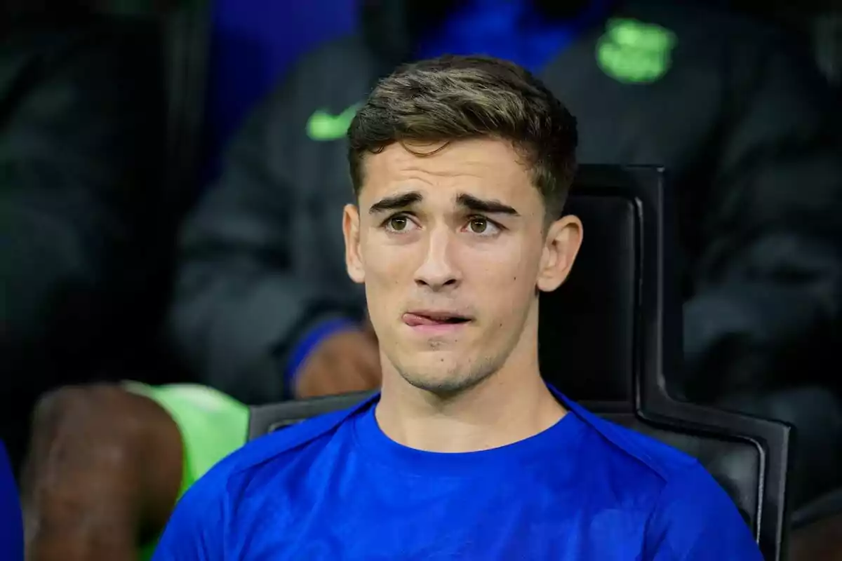 Jove futbolista assegut a la banqueta amb expressió pensativa i samarreta blava Jove futbolista assegut a la banqueta amb expressió pensativa i samarreta blava