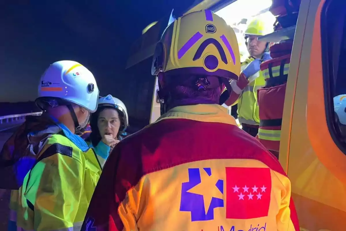 Personal d’emergències amb cascos i armilles reflectants conversa al costat d’una ambulància durant la nit Personal d’emergències amb cascos i armilles reflectants conversa al costat d’una ambulància durant la nit