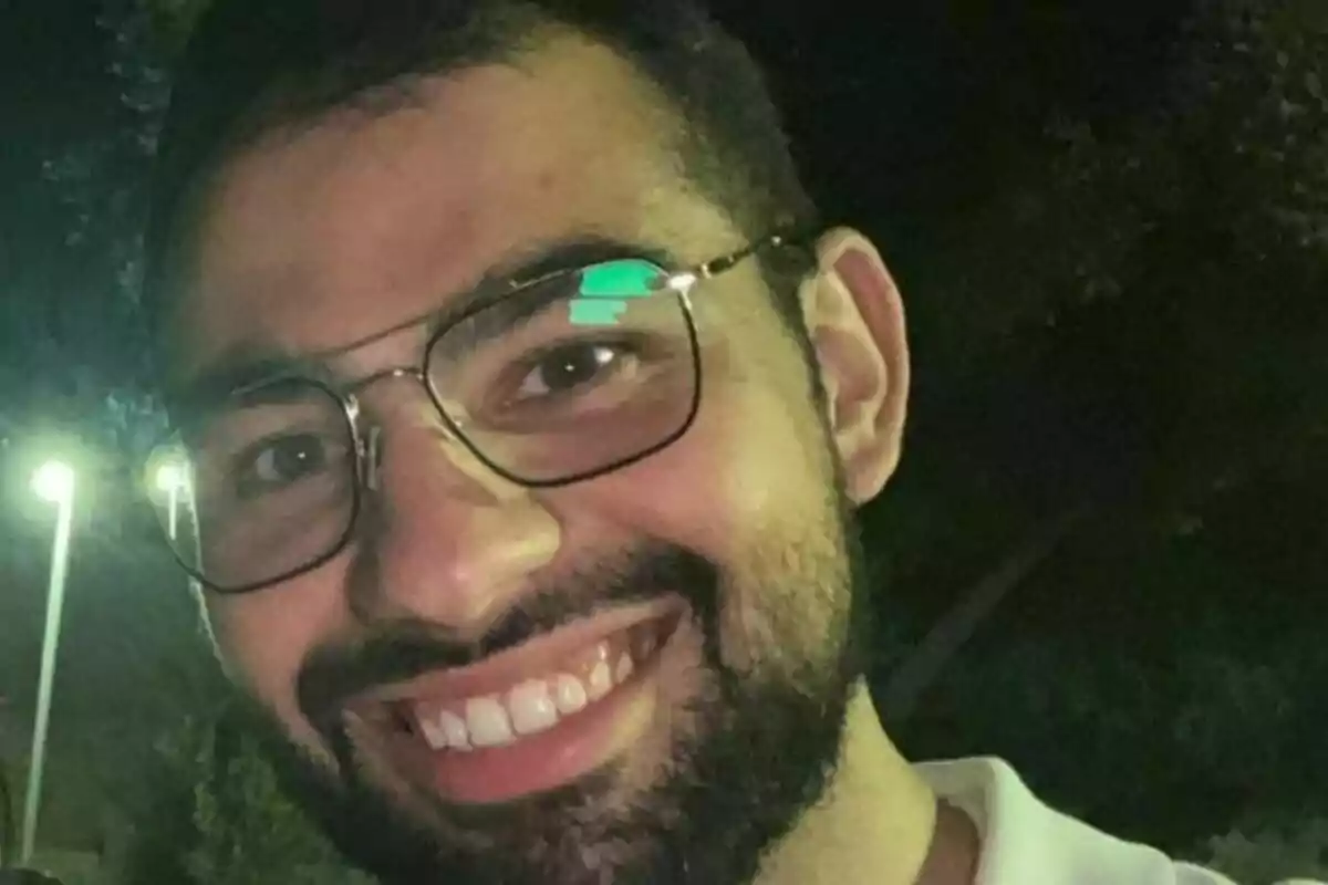 Home jove amb barba i ulleres somrient en un entorn nocturn a l’aire lliure