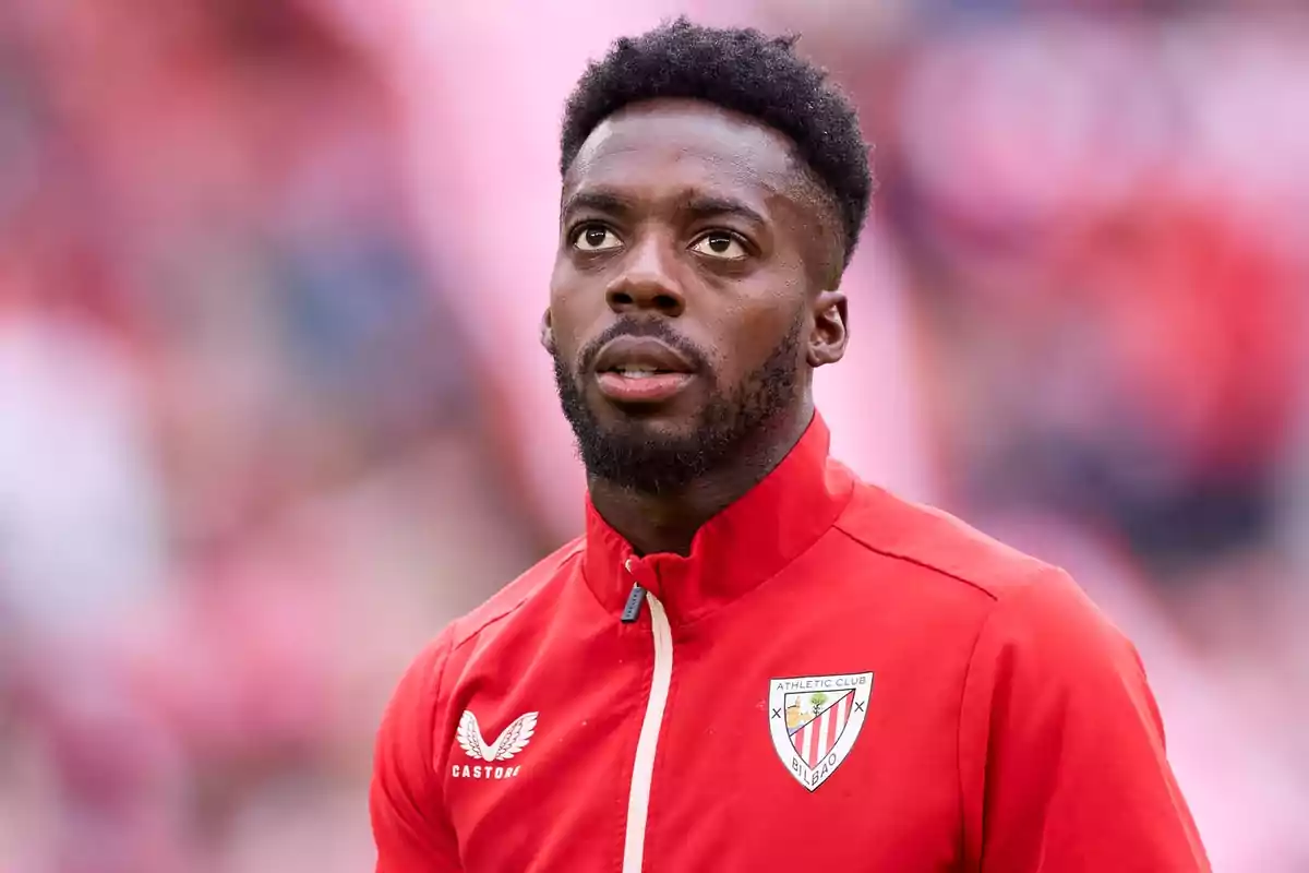 Iñaki Williams amb jaqueta vermella de l’Athletic Club de Bilbao mirant cap amunt en un estadi desenfocat