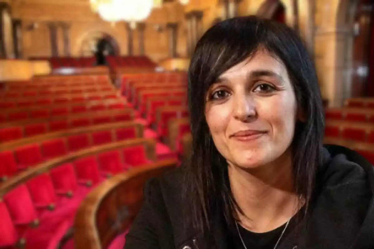 Dona de cabells foscos i llisos somrient en primer pla amb un auditori de seients vermells desenfocat al fons