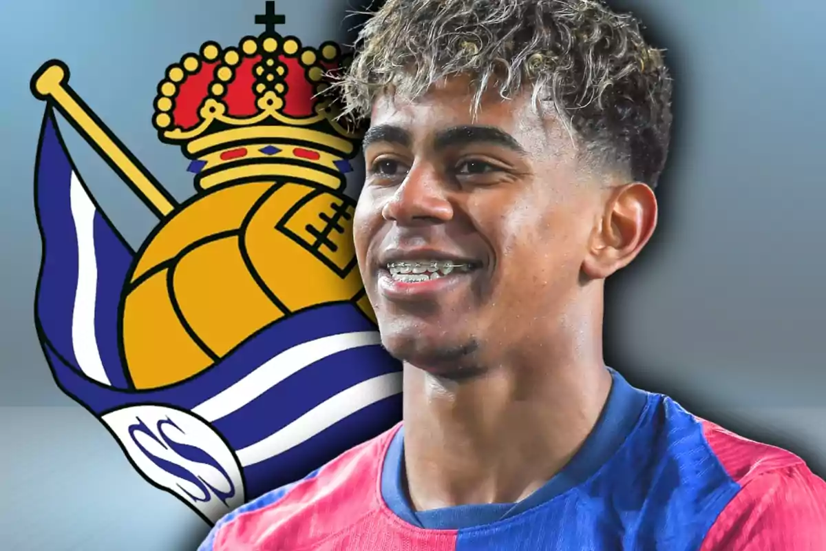 Joven futbolista sonriente con camiseta azul y roja frente al escudo de la Real Sociedad
