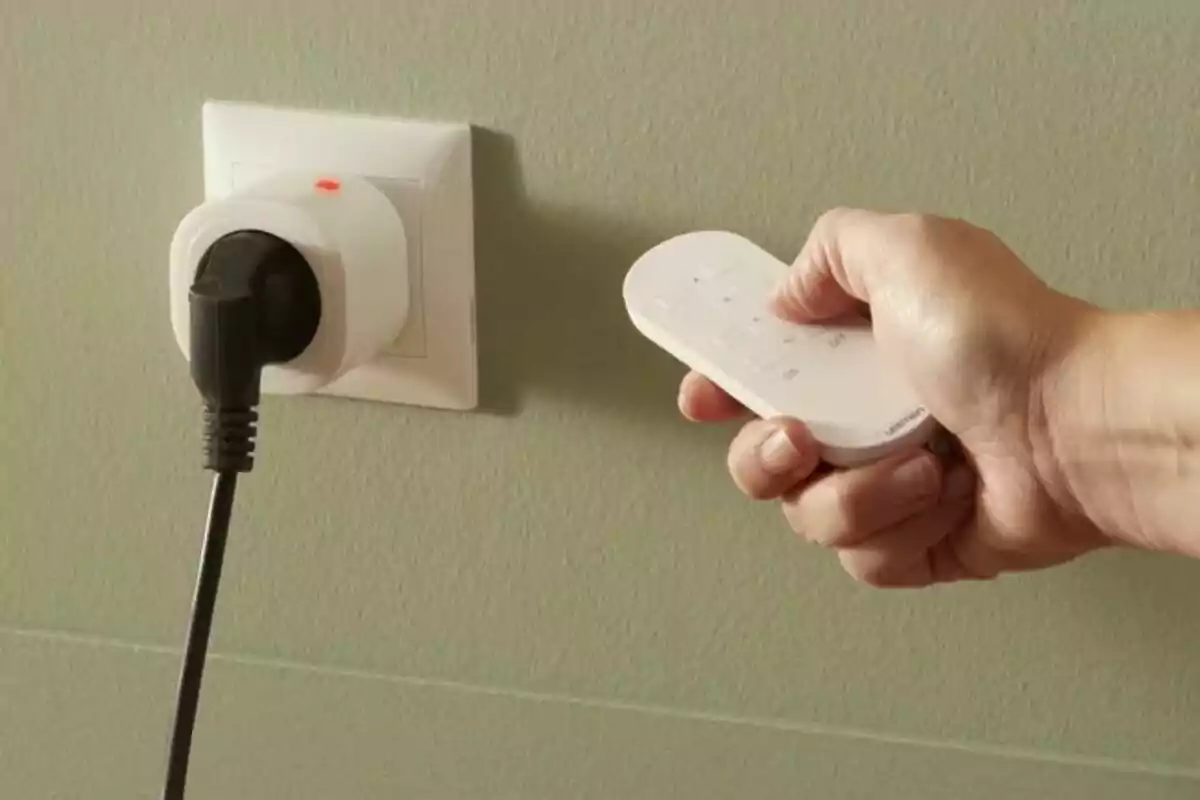 Persona usando un control remoto para operar un enchufe inteligente conectado a una toma de corriente en la pared