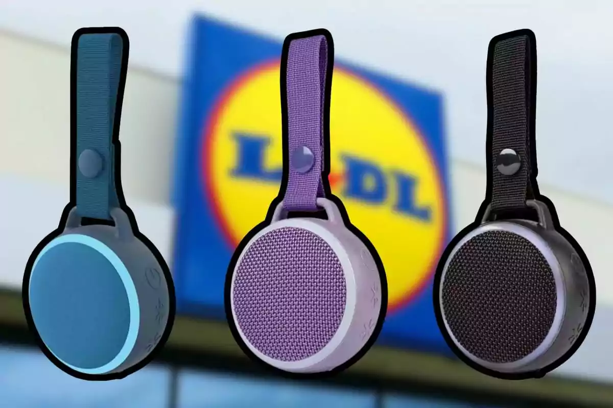 Tres altavoces portátiles de diferentes colores con correa están frente a un cartel borroso de la tienda Lidl