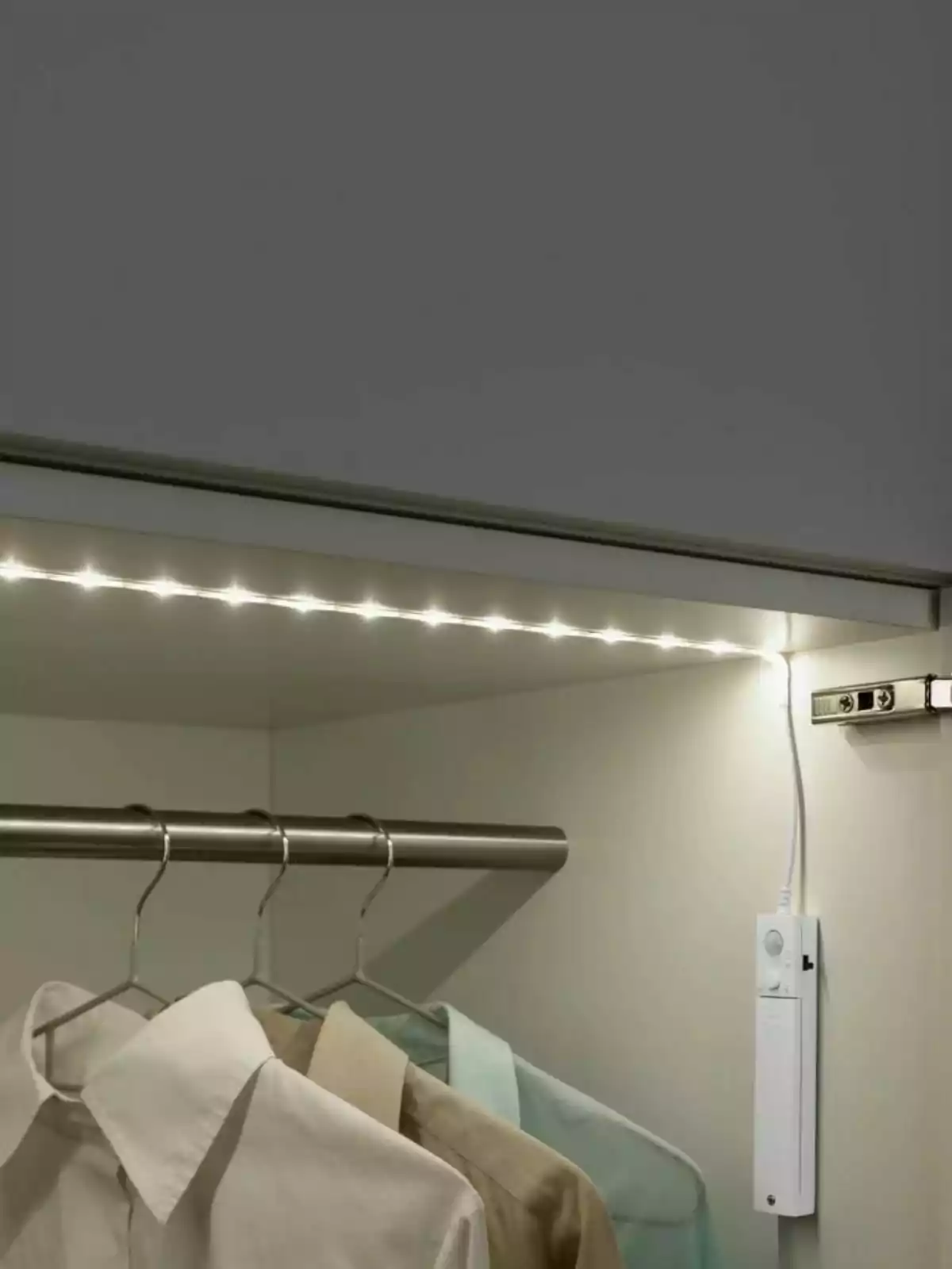 Clothes hanging in a closet lit by an LED strip and a sensor on the wall.