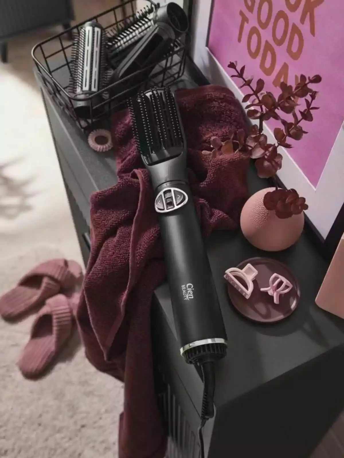 Cepillo secador negro sobre una toalla color vino junto a pinzas para el cabello, una planta decorativa, pantuflas y un cartel motivacional en un ambiente de tocador. Cepillo secador negro sobre una toalla color vino junto a pinzas para el cabello, una planta decorativa, pantuflas y un cartel motivacional en un ambiente de tocador.
