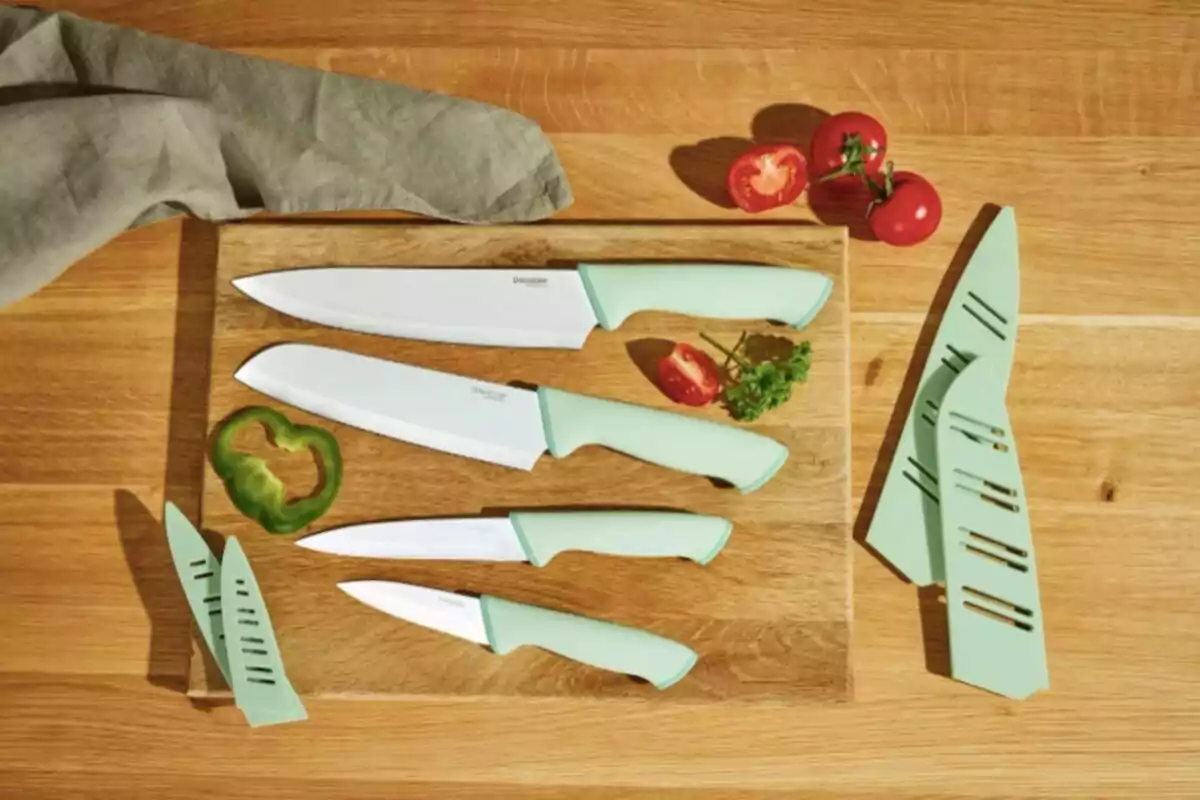Four kitchen knives with green handles on a wooden board next to protective sheaths, tomato slices, a green bell pepper, and a gray cloth Four kitchen knives with green handles on a wooden board next to protective sheaths, tomato slices, a green bell pepper, and a gray cloth
