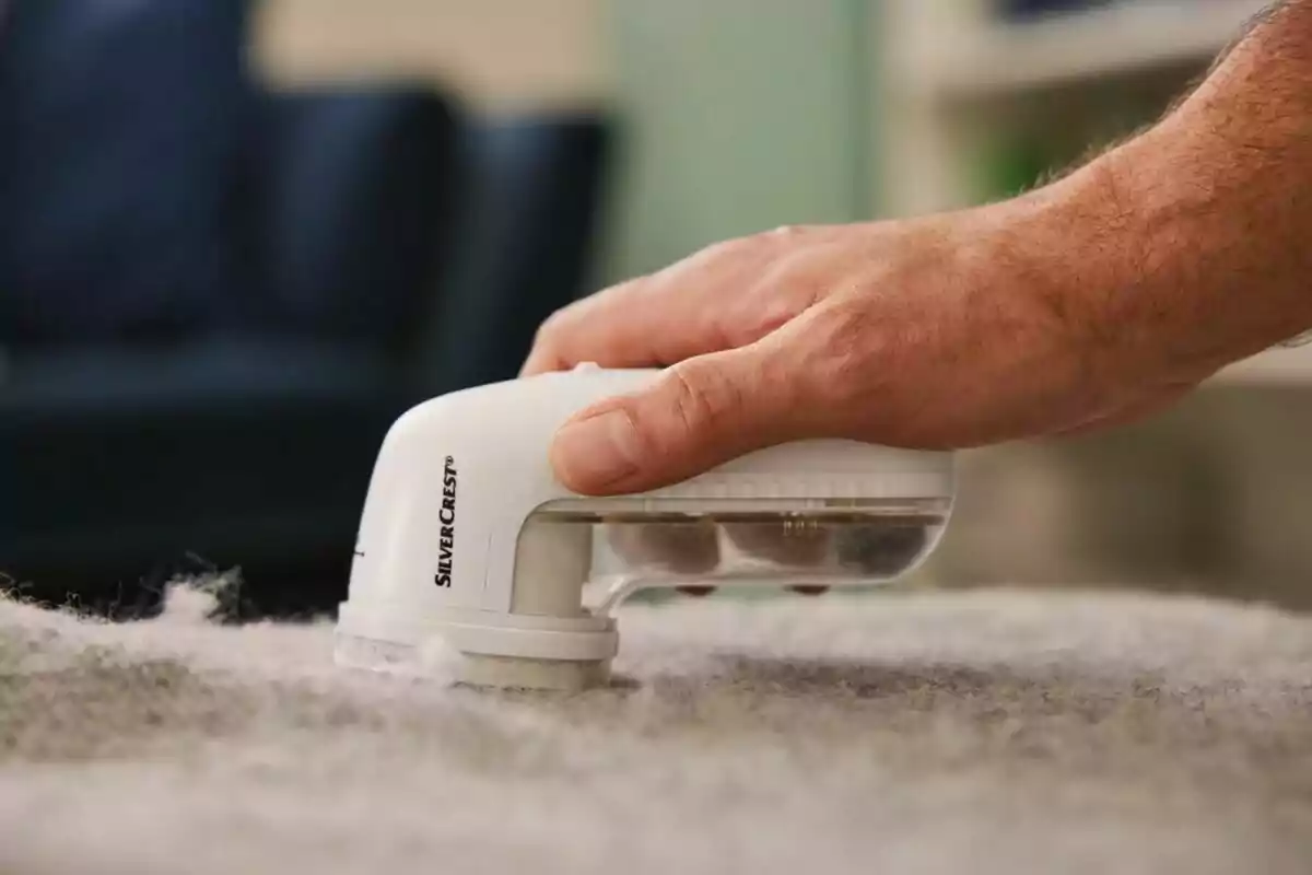 Mano usando un quitapelusas eléctrico sobre una prenda de tela gris