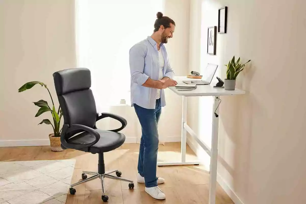 Man standing at a height-adjustable desk with a laptop and a decorative plant in a well-lit office Man standing at a height-adjustable desk with a laptop and a decorative plant in a well-lit office