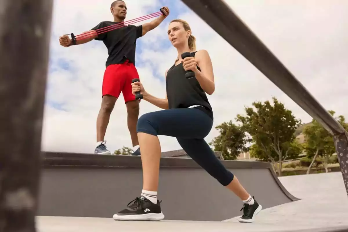 Dues persones fent exercici a l’aire lliure: una dona amb peses a les mans i un home utilitzant una banda elàstica de resistència.