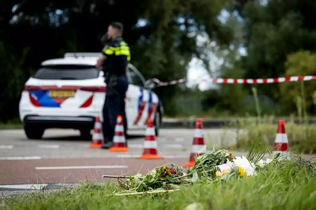 Ramo de flors a terra a prop d’una zona acordonada amb cons de trànsit i una patrulla de policia al fons Ramo de flors a terra a prop d’una zona acordonada amb cons de trànsit i una patrulla de policia al fons