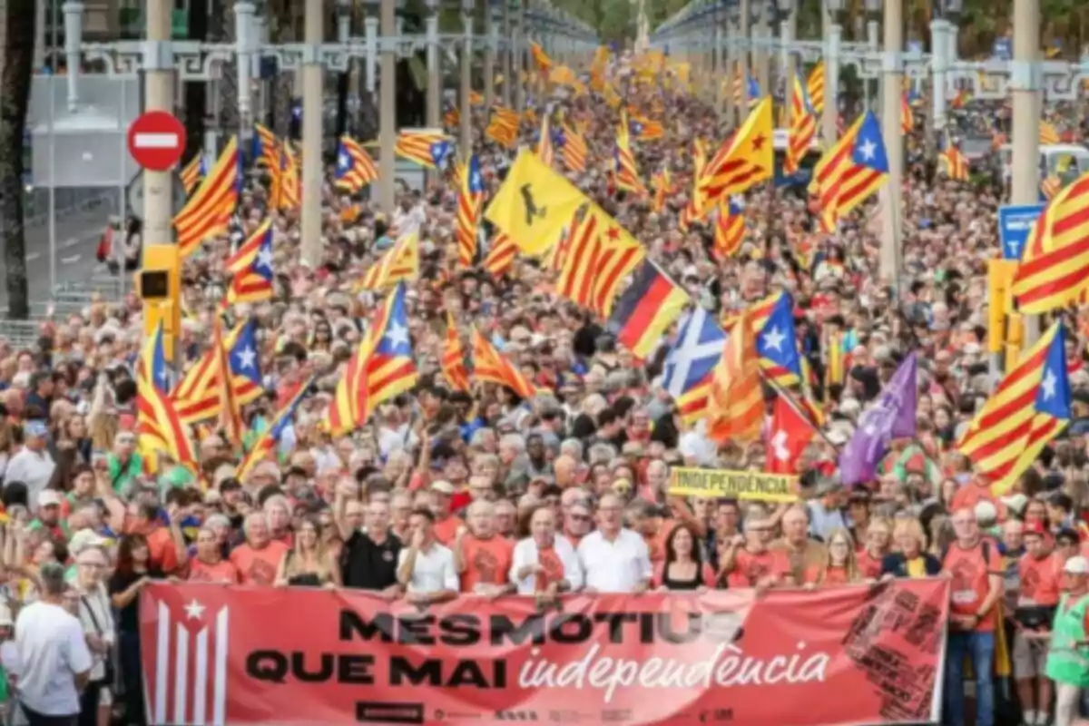 Multitud de personas marchando en una manifestación con banderas independentistas catalanas y una pancarta que dice més motius que mai independència Multitud de personas marchando en una manifestación con banderas independentistas catalanas y una pancarta que dice més motius que mai independència