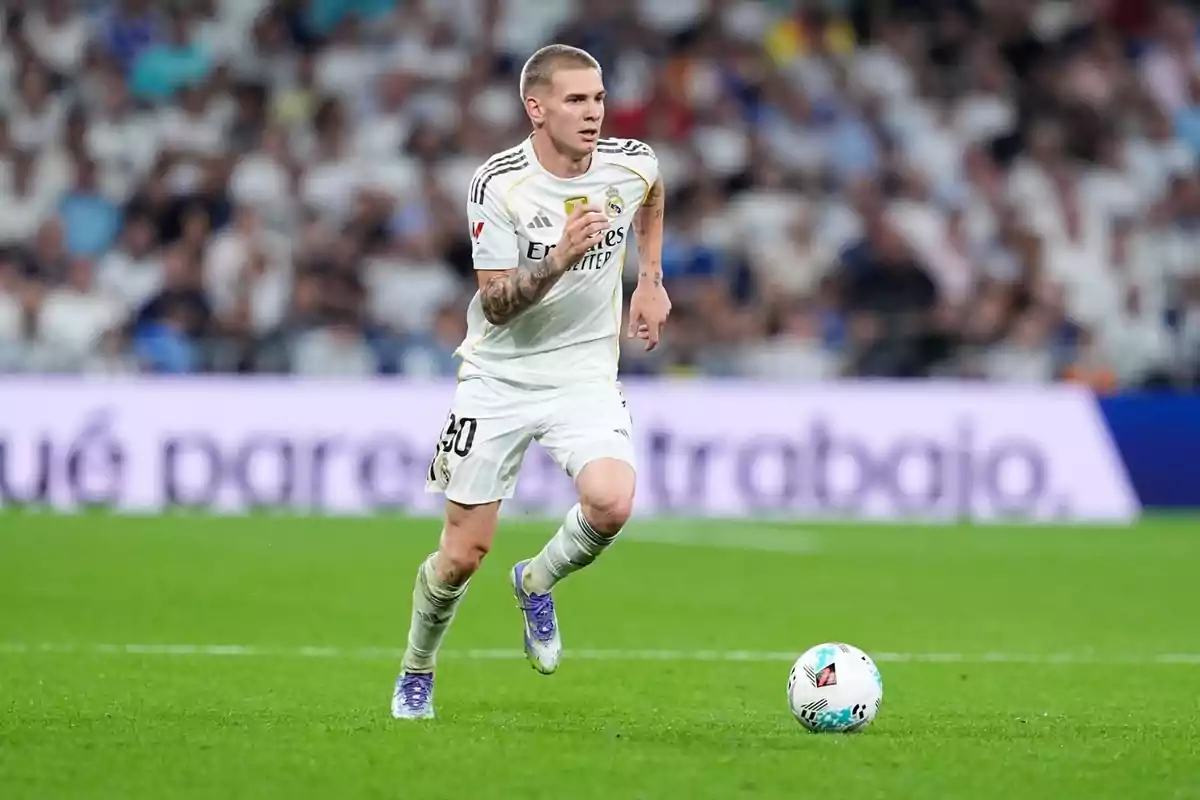 Futbolista del Real Madrid corriendo en el campo durante un partido con el balón cerca de sus pies y el público en las gradas de fondo Futbolista del Real Madrid corriendo en el campo durante un partido con el balón cerca de sus pies y el público en las gradas de fondo