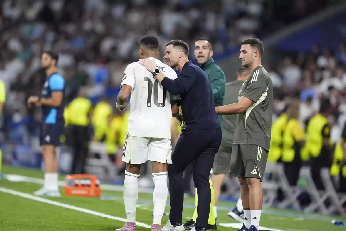 L’entrenador dona indicacions a un jugador amb el número 10 durant un partit de futbol mentre altres membres del cos tècnic observen a la banda.