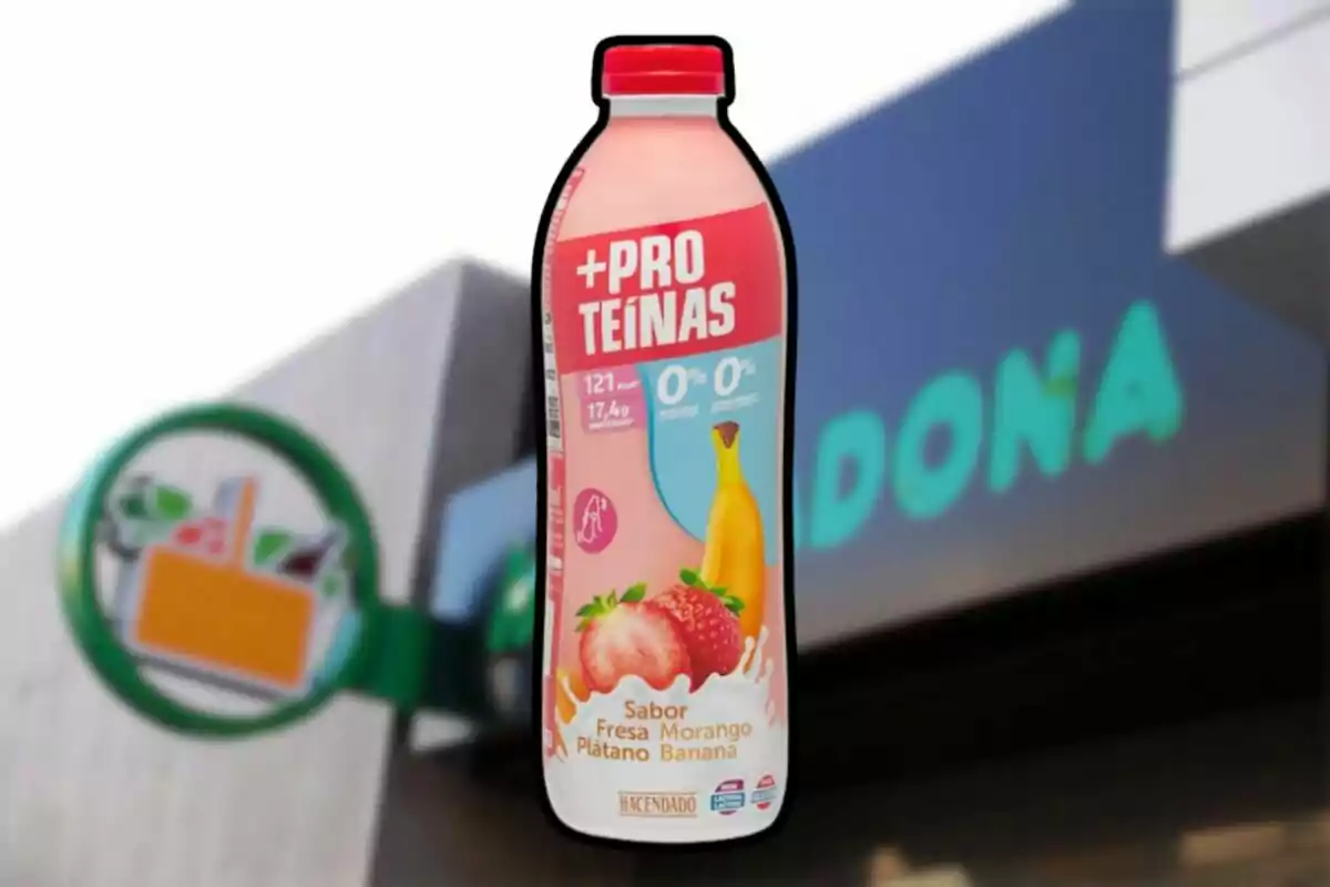 Ampolla de batut de proteïnes sabor maduixa i plàtan de la marca Hacendado davant d’una botiga Mercadona desenfocada