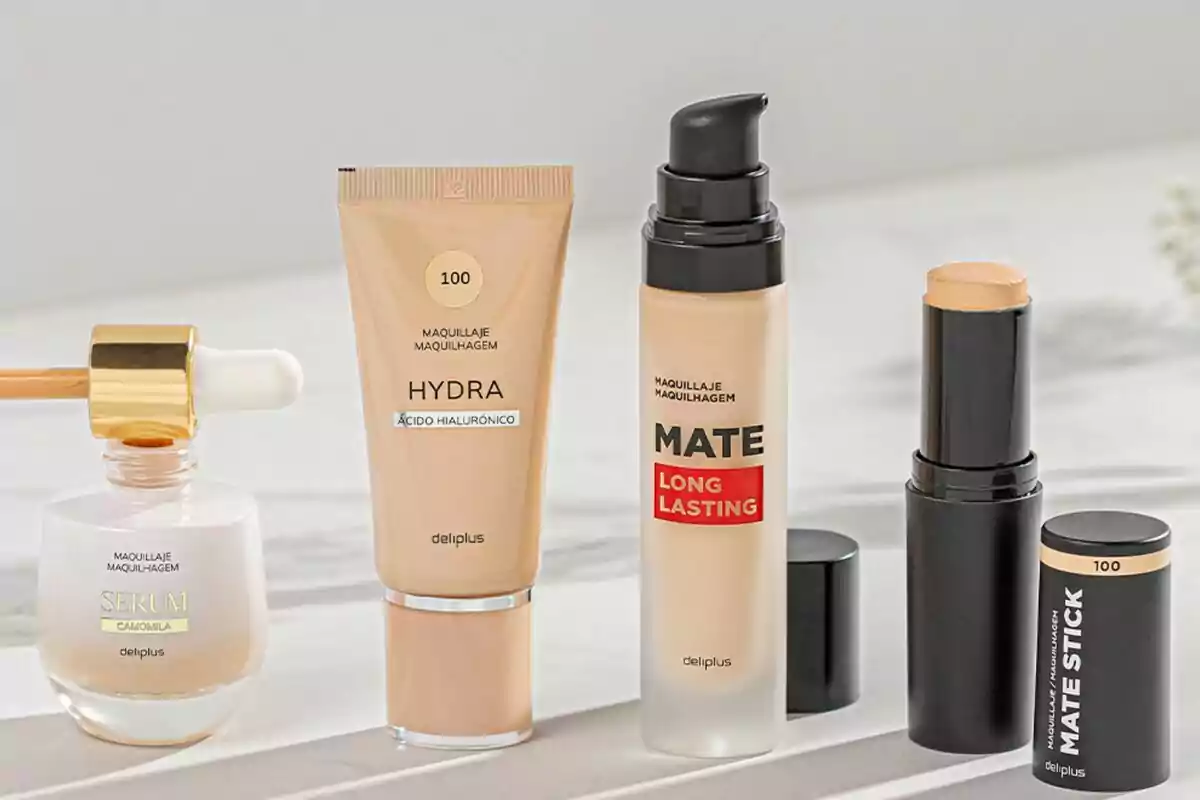 Cuatro productos de maquillaje Deliplus en diferentes formatos, incluyendo un sérum con gotero, una base líquida Hydra, una base Mate Long Lasting con dispensador y una base en barra Mate Stick, todos en tonos claros sobre una superficie blanca.