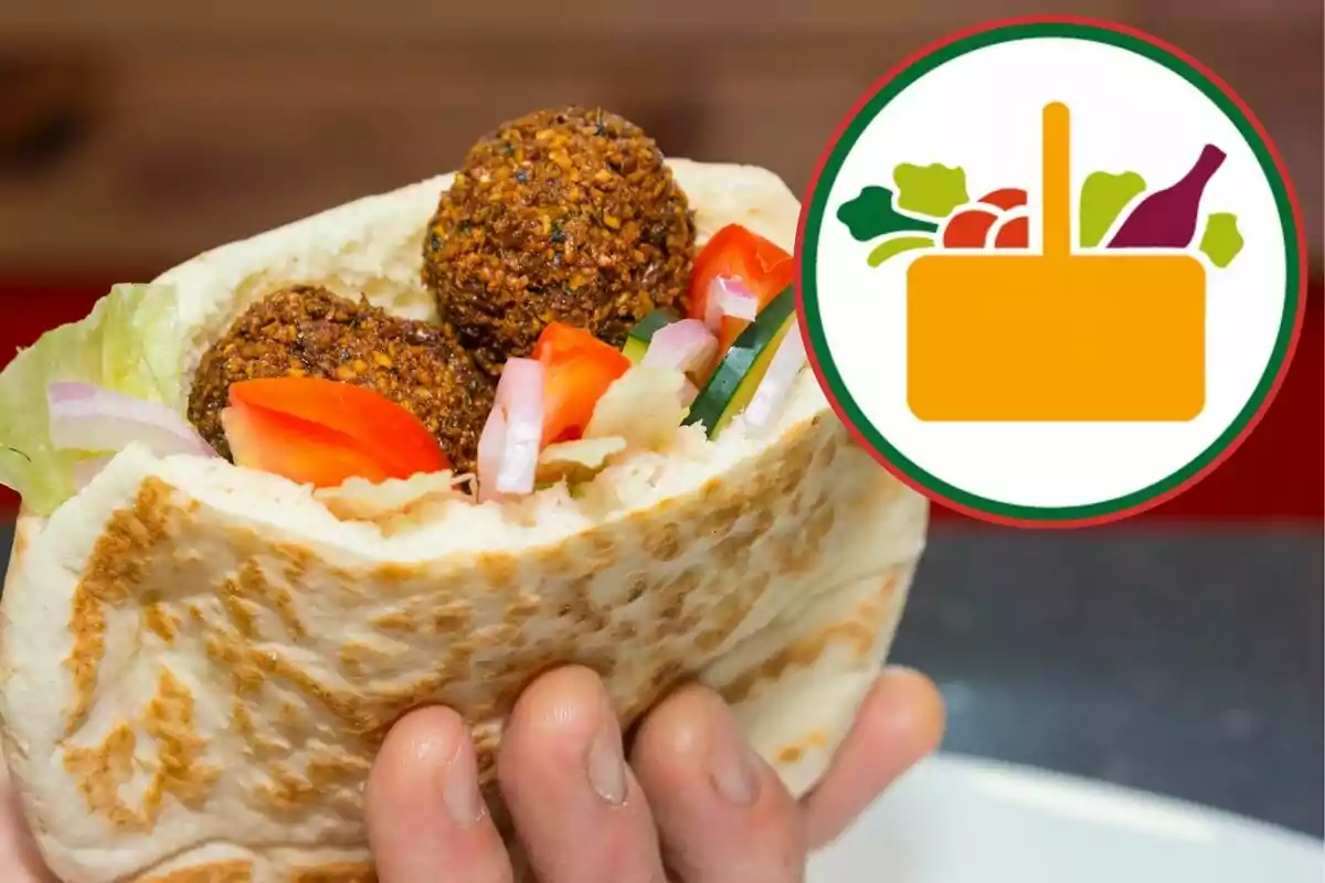 Persona sosteniendo un pan pita relleno de falafel, lechuga, jitomate, pepino y cebolla con un ícono de canasta de alimentos al fondo