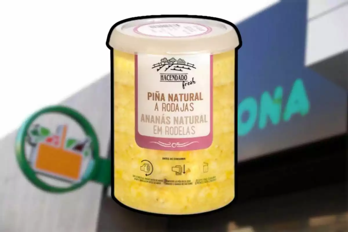 Envàs de pinya natural en rodanxes de la marca Hacendado davant d’un cartell de supermercat Mercadona desenfocat Envàs de pinya natural en rodanxes de la marca Hacendado davant d’un cartell de supermercat Mercadona desenfocat