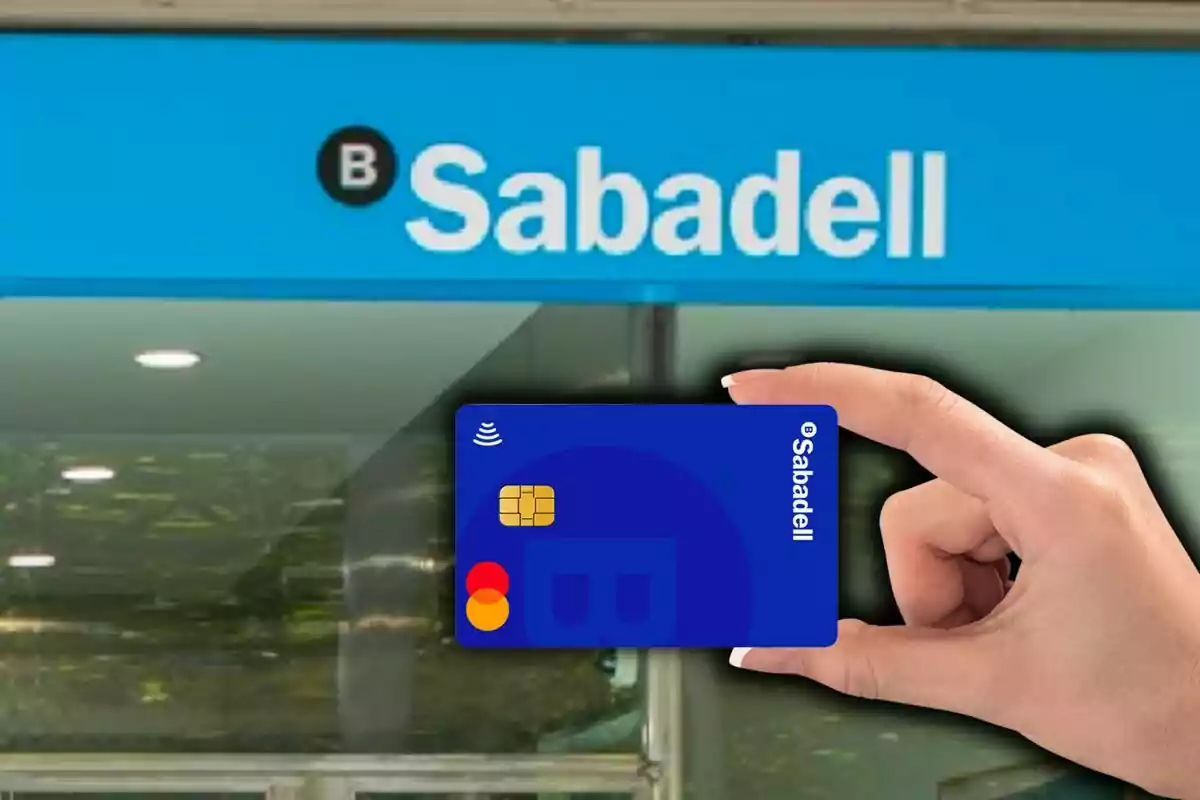 Una mà sosté una targeta bancària blava de Sabadell davant d’una sucursal del banc. Una mà sosté una targeta bancària blava de Sabadell davant d’una sucursal del banc.