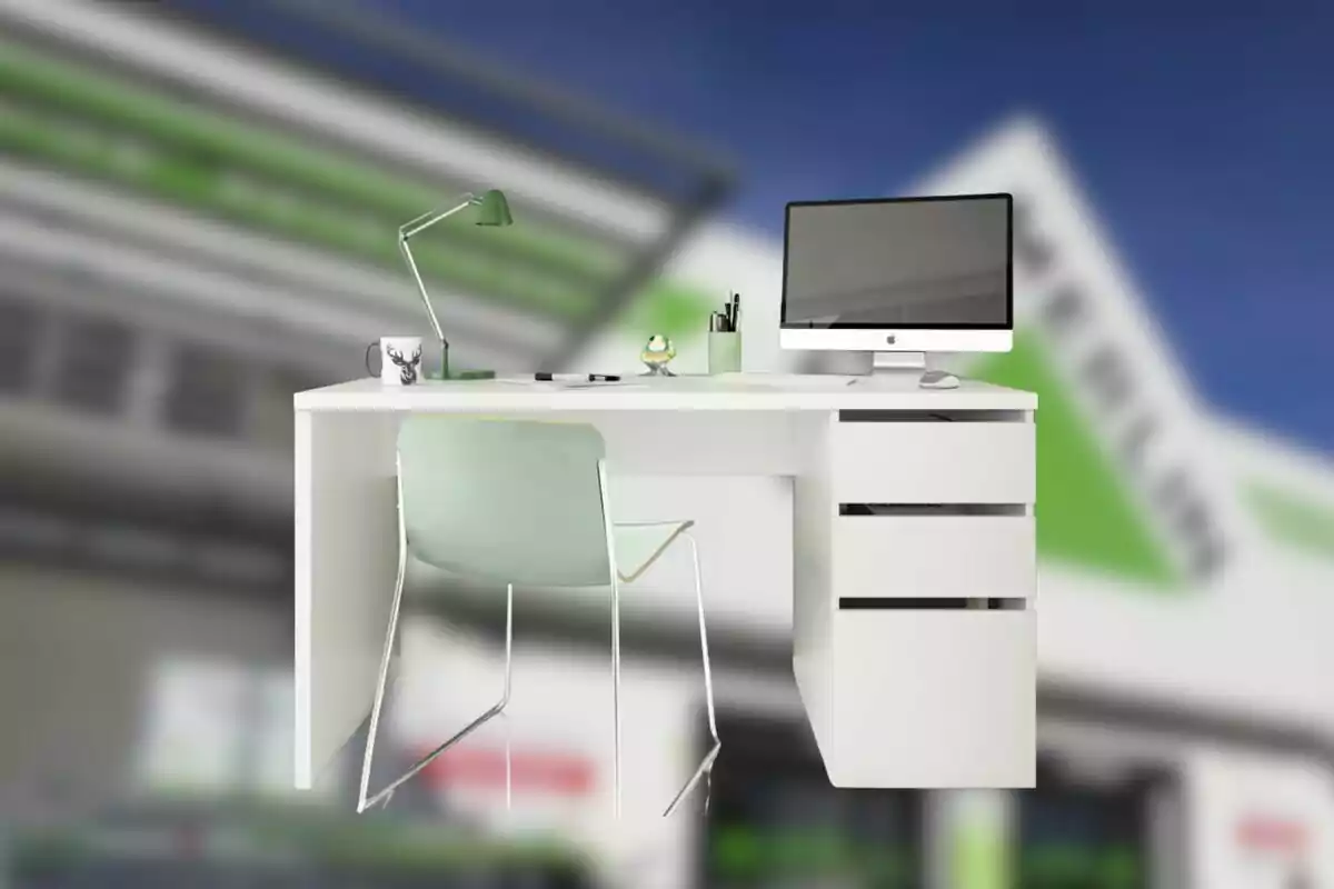 Escritorio blanco con cajones, silla verde claro, lámpara, computadora y artículos de oficina sobre un fondo desenfocado de edificio.