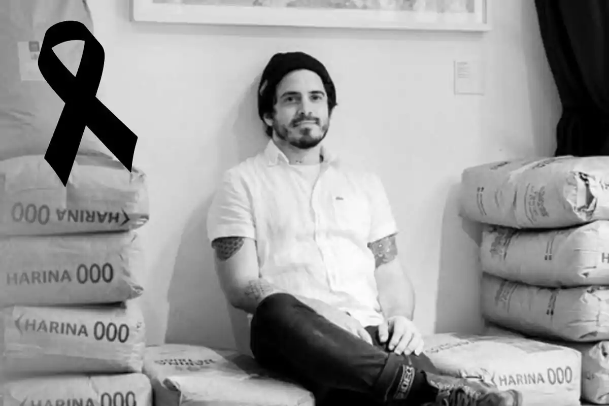 Hombre sentado sobre sacos de harina en una habitación, con un lazo negro de luto en la esquina de la imagen