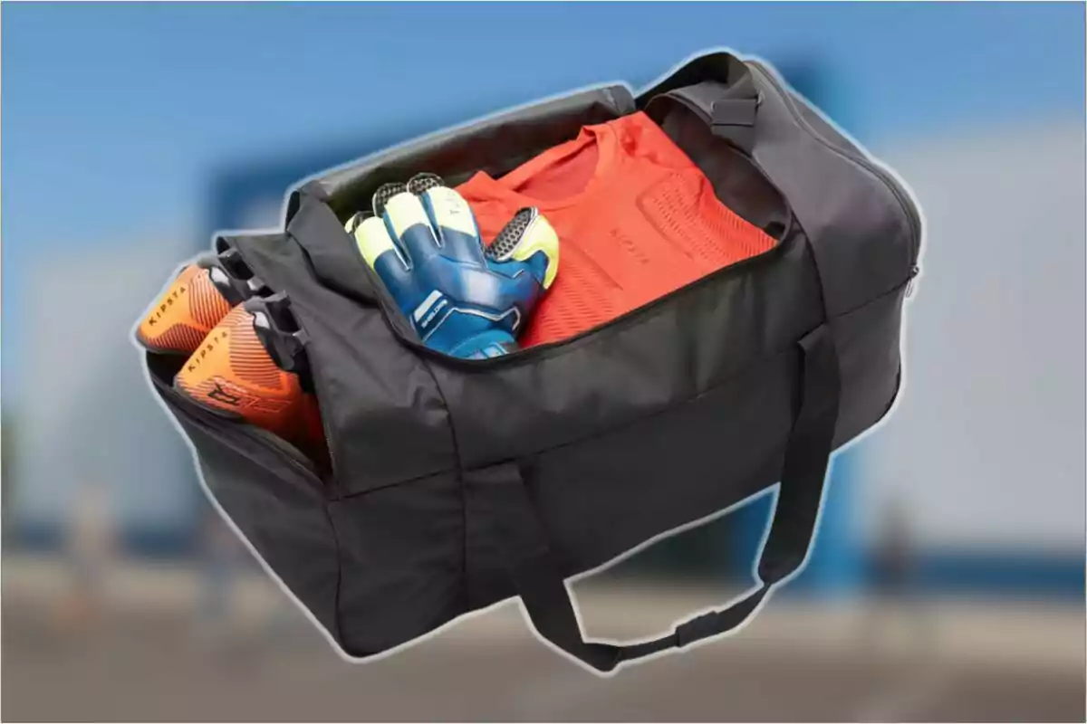 Bolsa deportiva negra abierta con un uniforme rojo, guantes de portero y zapatos de fútbol en su interior