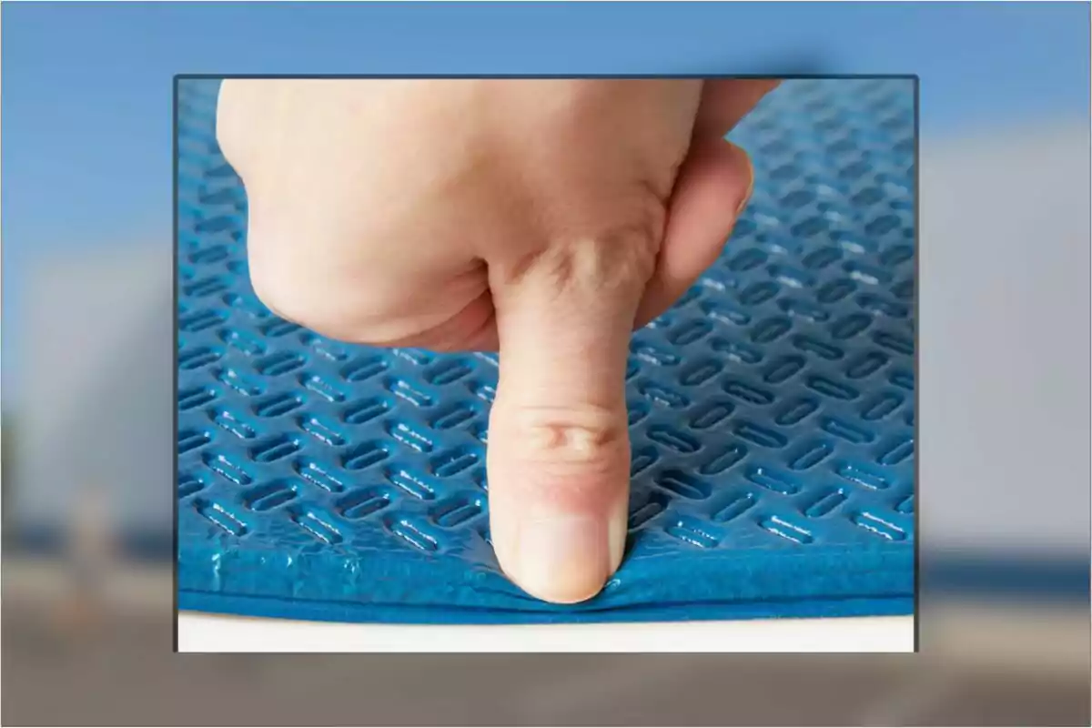 Dit pressionant una superfície blava encoixinada amb textura geomètrica Dit pressionant una superfície blava encoixinada amb textura geomètrica