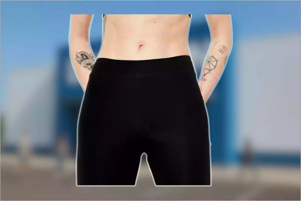 Persona con tatuajes en los brazos usando leggings negros frente a un fondo desenfocado.