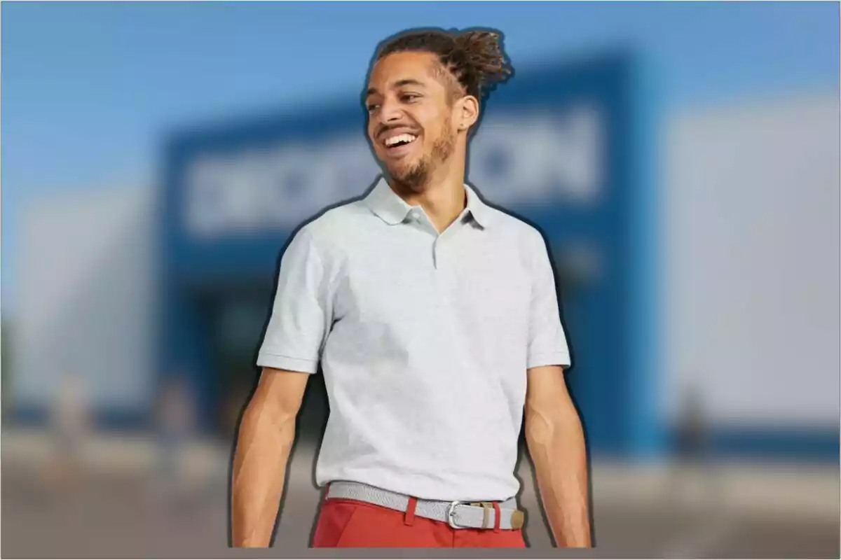 Hombre joven sonriente con camiseta tipo polo gris y pantalón rojo de pie frente a un edificio azul desenfocado Hombre joven sonriente con camiseta tipo polo gris y pantalón rojo de pie frente a un edificio azul desenfocado