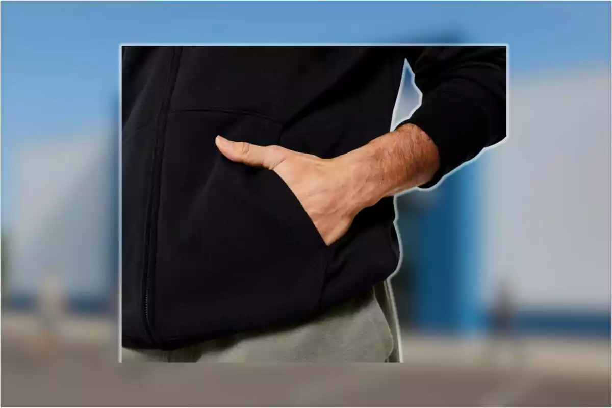 Persona con sudadera negra y pantalón gris mete la mano en el bolsillo delantero de la prenda.