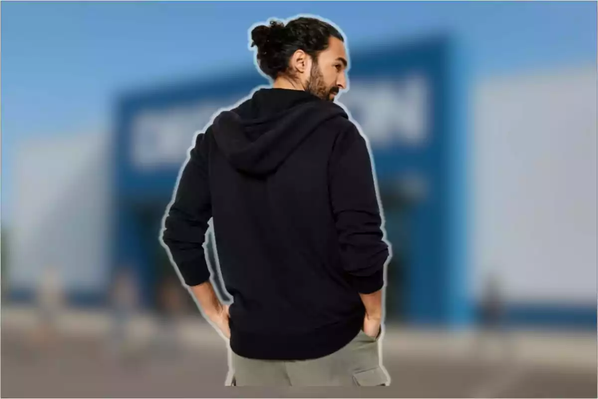 Hombre de espaldas con sudadera negra y pantalón claro frente a un edificio azul desenfocado