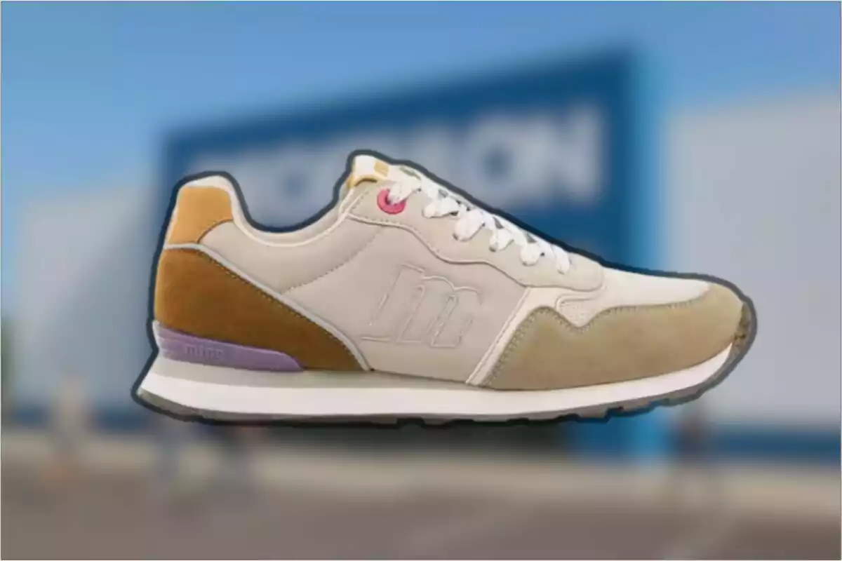 Zapatilla deportiva beige con detalles en marrón y lila sobre un fondo desenfocado azul