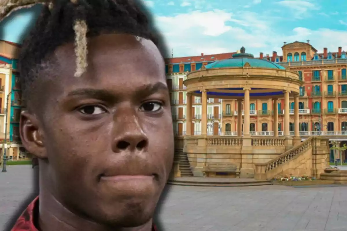 Primer pla de Nico Williams amb expressió seriosa davant d’un quiosc en una plaça envoltada d’edificis antics