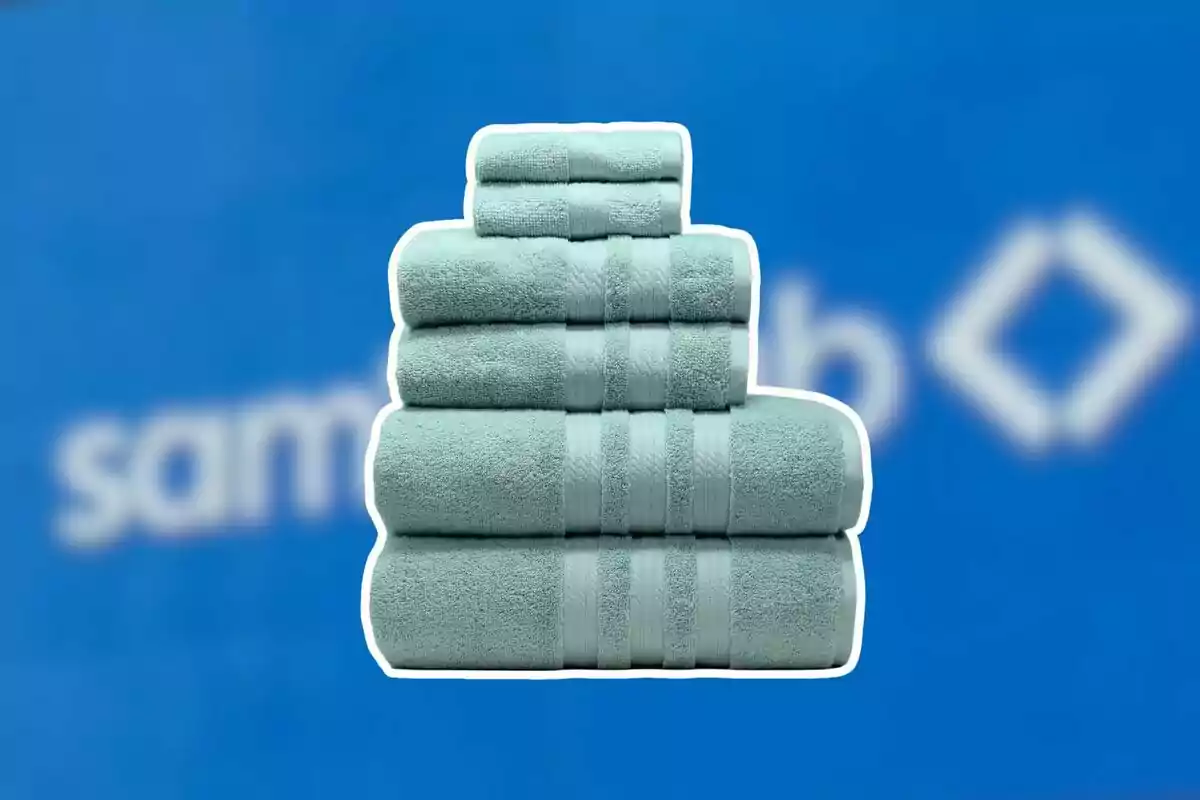 Un juego de toallas color verde menta apiladas frente a un fondo azul con letras borrosas