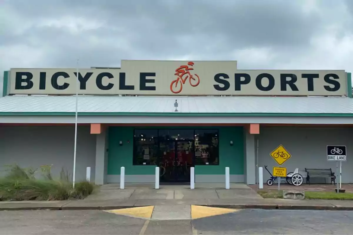 Fachada de una tienda de bicicletas llamada Bicycle Sports con señales de ciclovía y un triciclo decorativo afuera