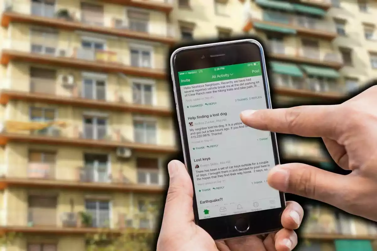 Persona utilitzant un telèfon intel·ligent davant d’un edifici d’apartaments mentre navega per una aplicació de barri