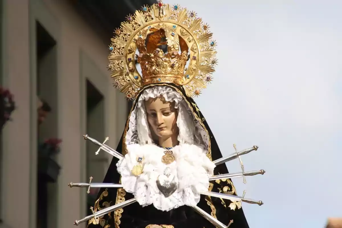 Imagen de una figura religiosa de la Virgen María vestida de negro con una corona dorada y siete espadas en el pecho, representando a la Virgen de los Dolores.