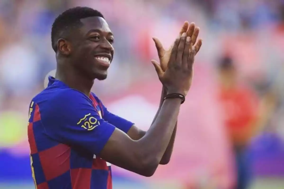 The player Ousmane Dembélé in a blue and red uniform clapping and smiling in a stadium The player Ousmane Dembélé in a blue and red uniform clapping and smiling in a stadium