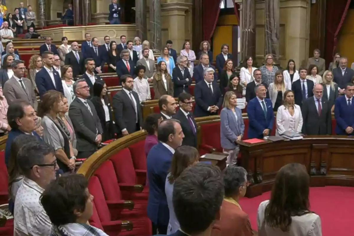Personas de pie en un parlamento con asientos rojos y ambiente formal