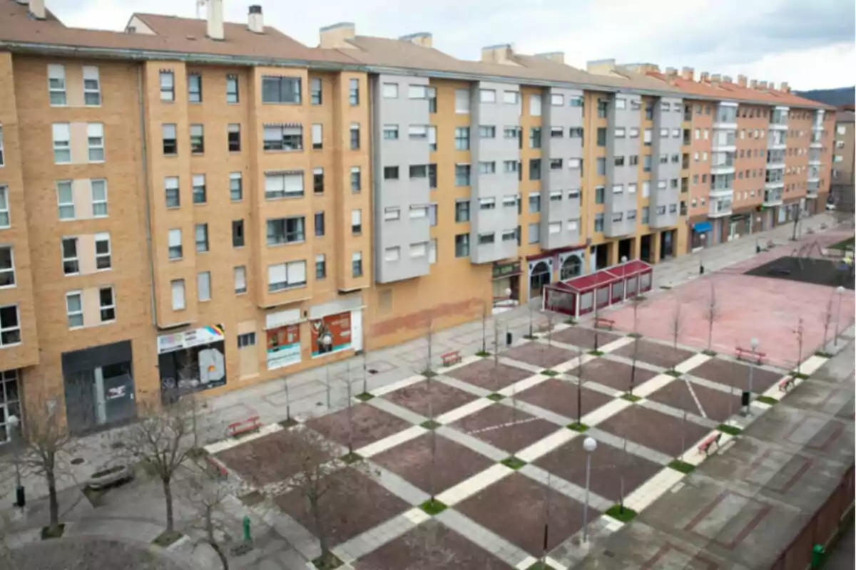 Plaça urbana amb bancs, arbres joves i edificis residencials al fons en un dia ennuvolat