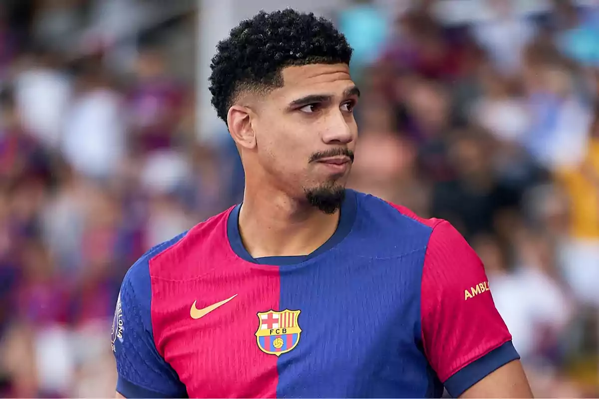 Futbolista Ronald Araújo amb la samarreta del FC Barcelona mirant cap a un costat en un estadi ple de públic desenfocat. Futbolista Ronald Araújo amb la samarreta del FC Barcelona mirant cap a un costat en un estadi ple de públic desenfocat.
