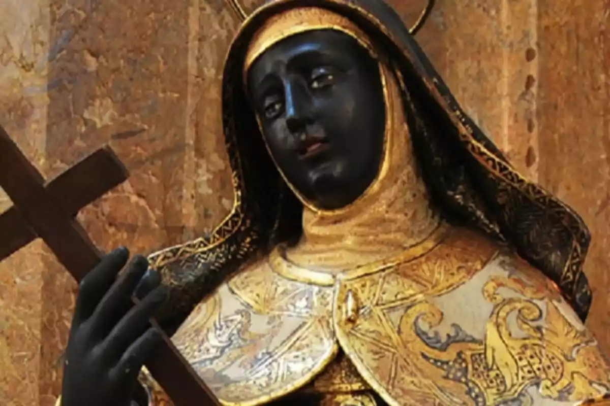 Escultura religiosa de una mujer con hábito y rostro oscuro sosteniendo una cruz en un fondo dorado Escultura religiosa de una mujer con hábito y rostro oscuro sosteniendo una cruz en un fondo dorado
